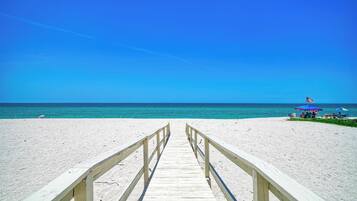 A wooden boardwalk leading to a beach with a clear blue sky.