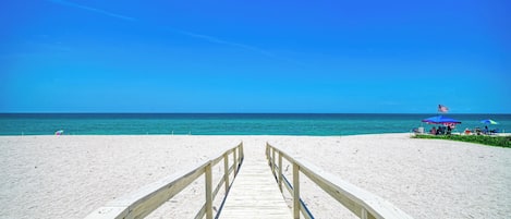 En träpromenad som leder till en strand med en klarblå himmel.