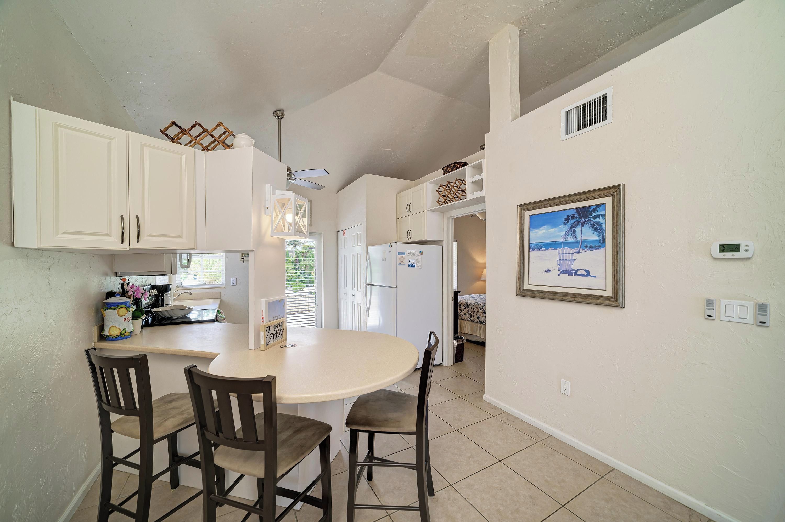 A kitchen with white cabinets, a central island with chairs, a refrigerator, and a painting on the wall.