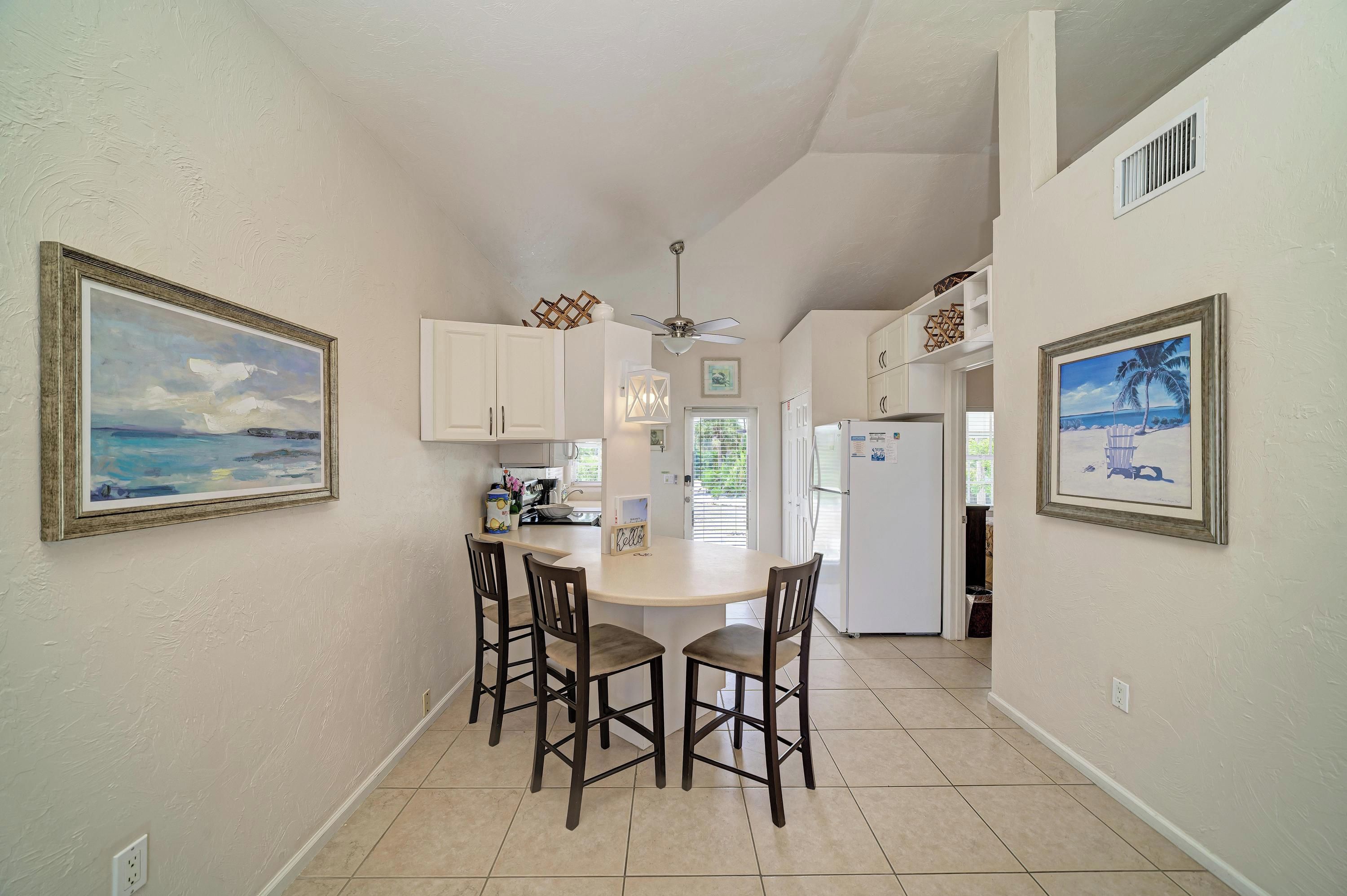 A kitchen with white cabinets, a dining area with four chairs, and two framed paintings on the walls.