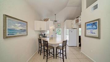 A kitchen with white cabinets, a dining area with four chairs, and two framed paintings on the walls.