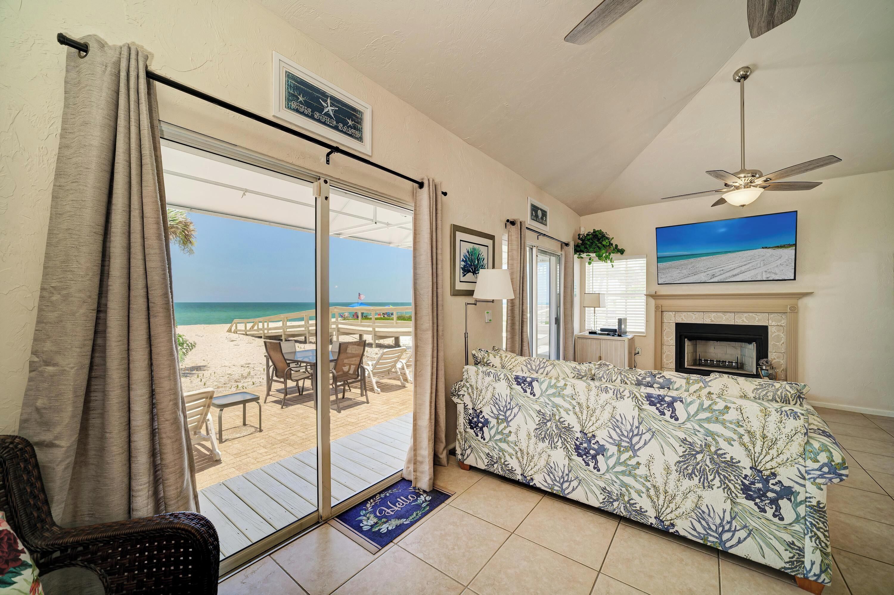 Habitación con vista a la playa, ventilador de techo, chimenea y zona de comedor con asientos exteriores.
