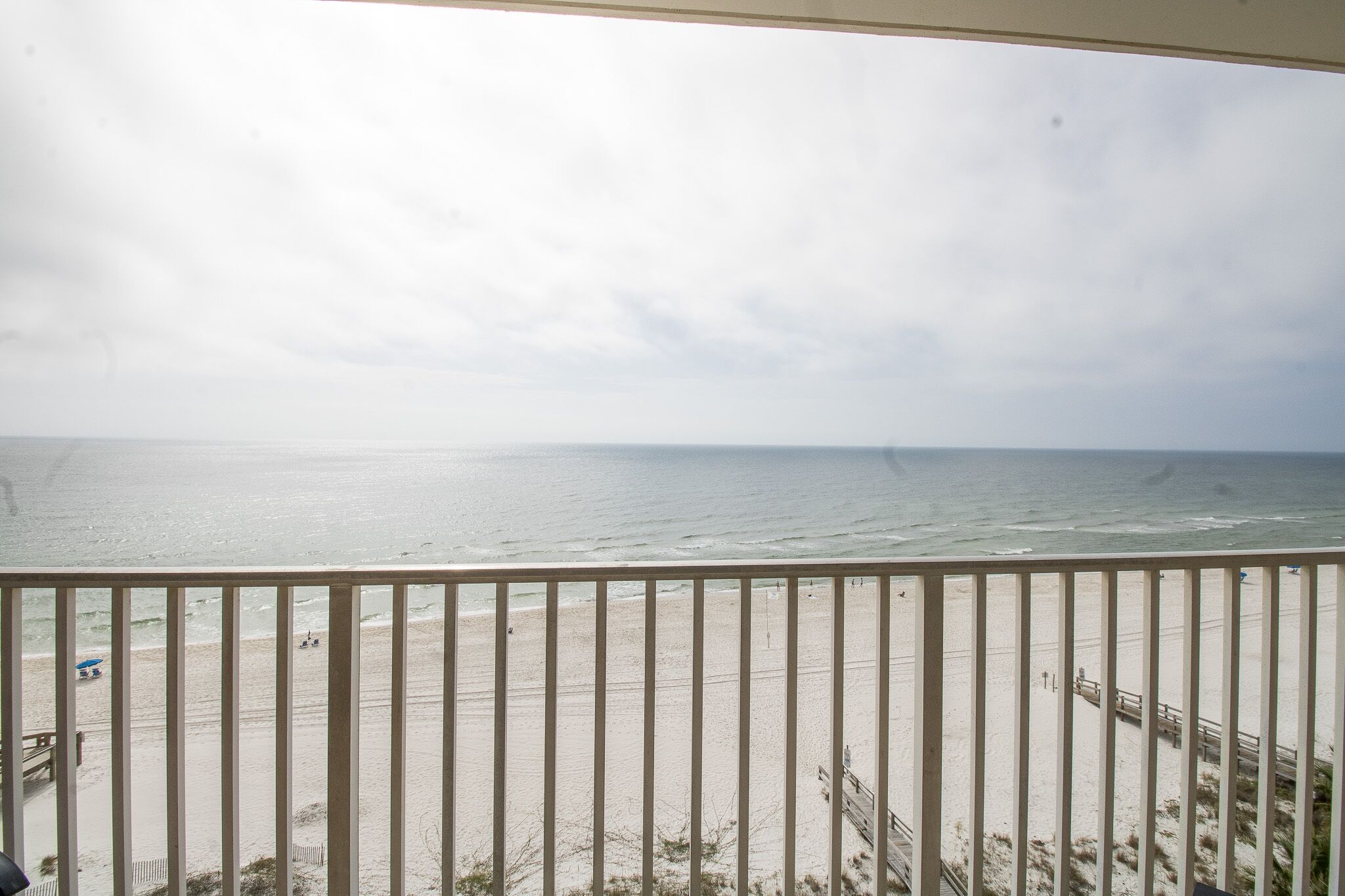 A beach view from a balcony with a railing, sandy beach, and ocean.