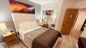 A bedroom with a large bed, a nightstand, a bedside table with a lamp, a mirror, and a wooden door. - Loft Escape Artistic (Surprise)