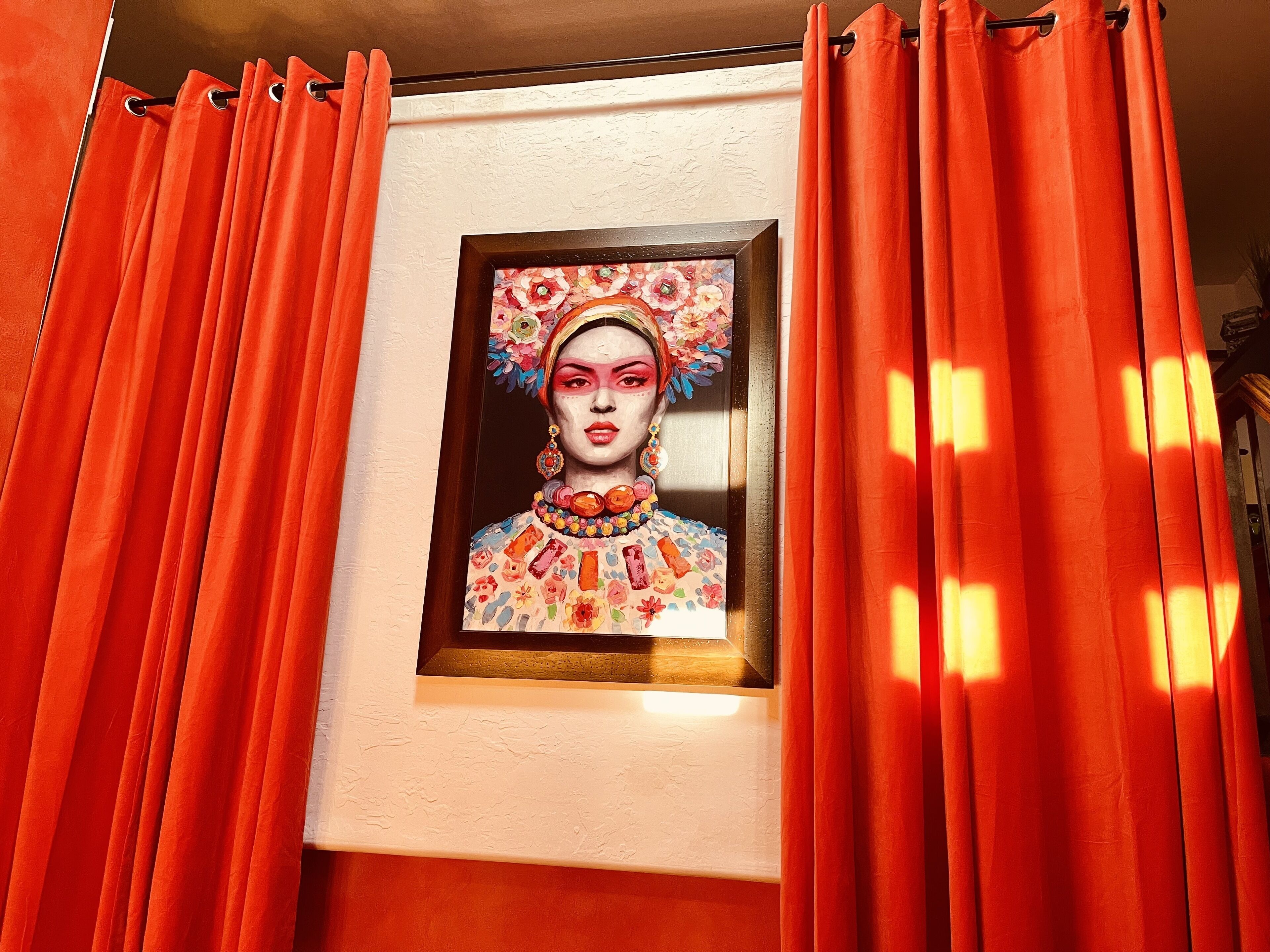 A framed artwork on a wall, surrounded by orange curtains.