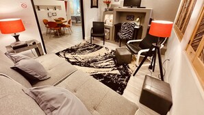 A modern living room with a sofa, armchairs, a coffee table, and a TV. There is a fireplace with a zebra-patterned chair, and a dining area in the background. - Loft Escape Artistic (Surprise)