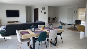 Uma sala de estar moderna com área de jantar, um sofá e uma TV fixada na parede.
