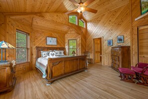 Une chambre à coucher dans un chalet en bois, avec un lit, une commode, des fauteuils à bascule et un ventilateur de plafond.