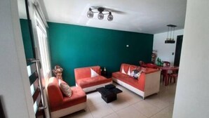 Una sala de estar con dos sofás rojos, un ventilador de techo y un comedor con mesa y sillas.