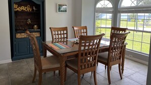 A dining area with a table and four chairs, a blue cabinet with decorative items, and a view of the outdoors through large windows. - 3/2 with Heated Pool - Tranquil Tropical Escape
(Sebastian)