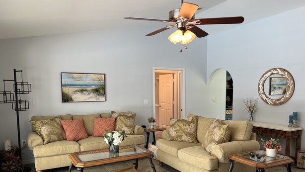 A living room with two sofas, a glass coffee table, a wooden side table, a ceiling fan, and a painting on the wall. - 3/2 with Heated Pool - Tranquil Tropical Escape
(Sebastian)