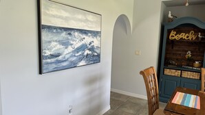 A dining area with a table and chairs, a wall-mounted painting of a seascape, and a blue cabinet labeled "Beach" with a clock and decorative items. - 3/2 with Heated Pool - Tranquil Tropical Escape
(Sebastian)