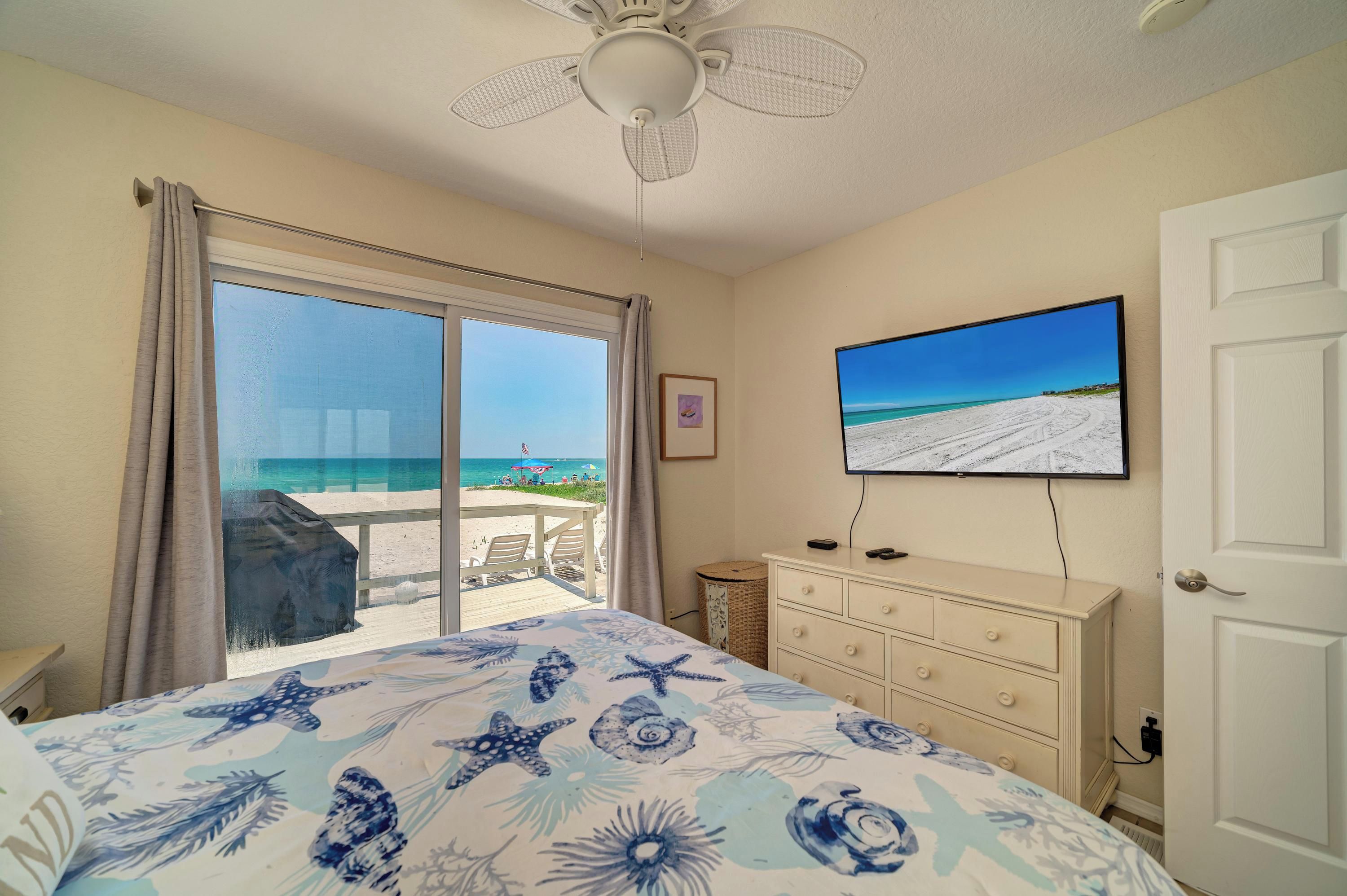 Quarto com vista para a praia, ventoinha no teto, televisão e cómoda.