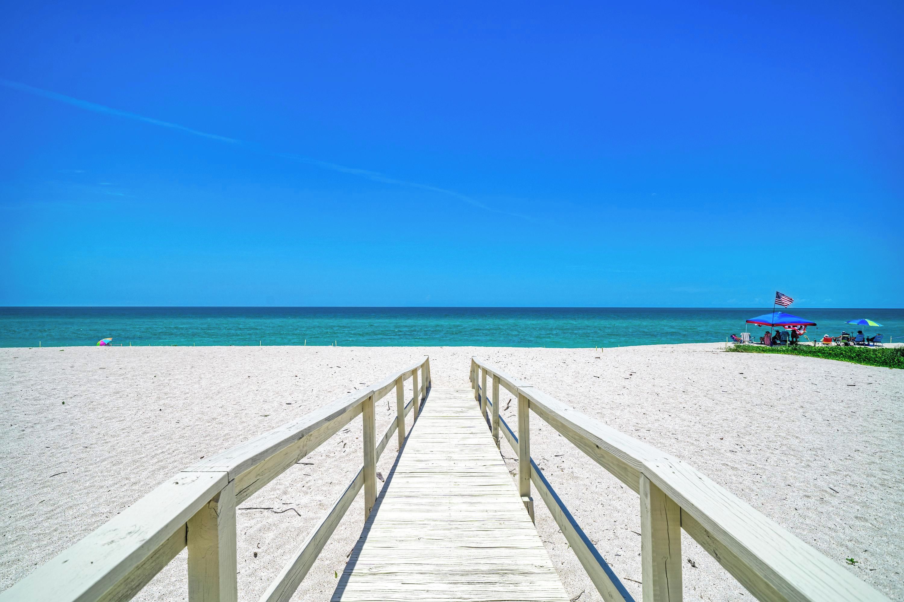 Une promenade en bois qui mène à une plage, avec un ciel bleu dégagé.
