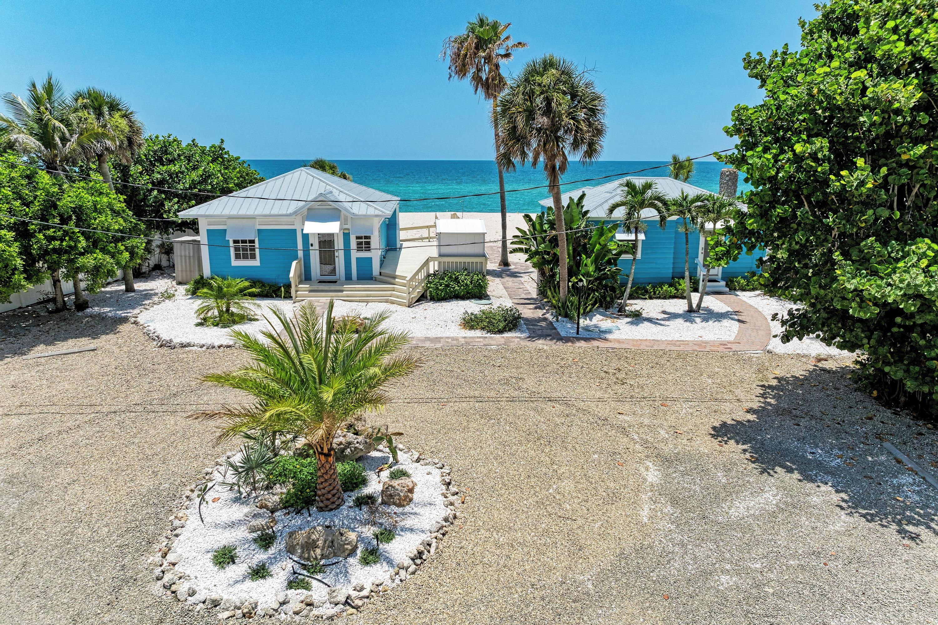 A beachfront property with a small house, a paved driveway, and a palm tree.