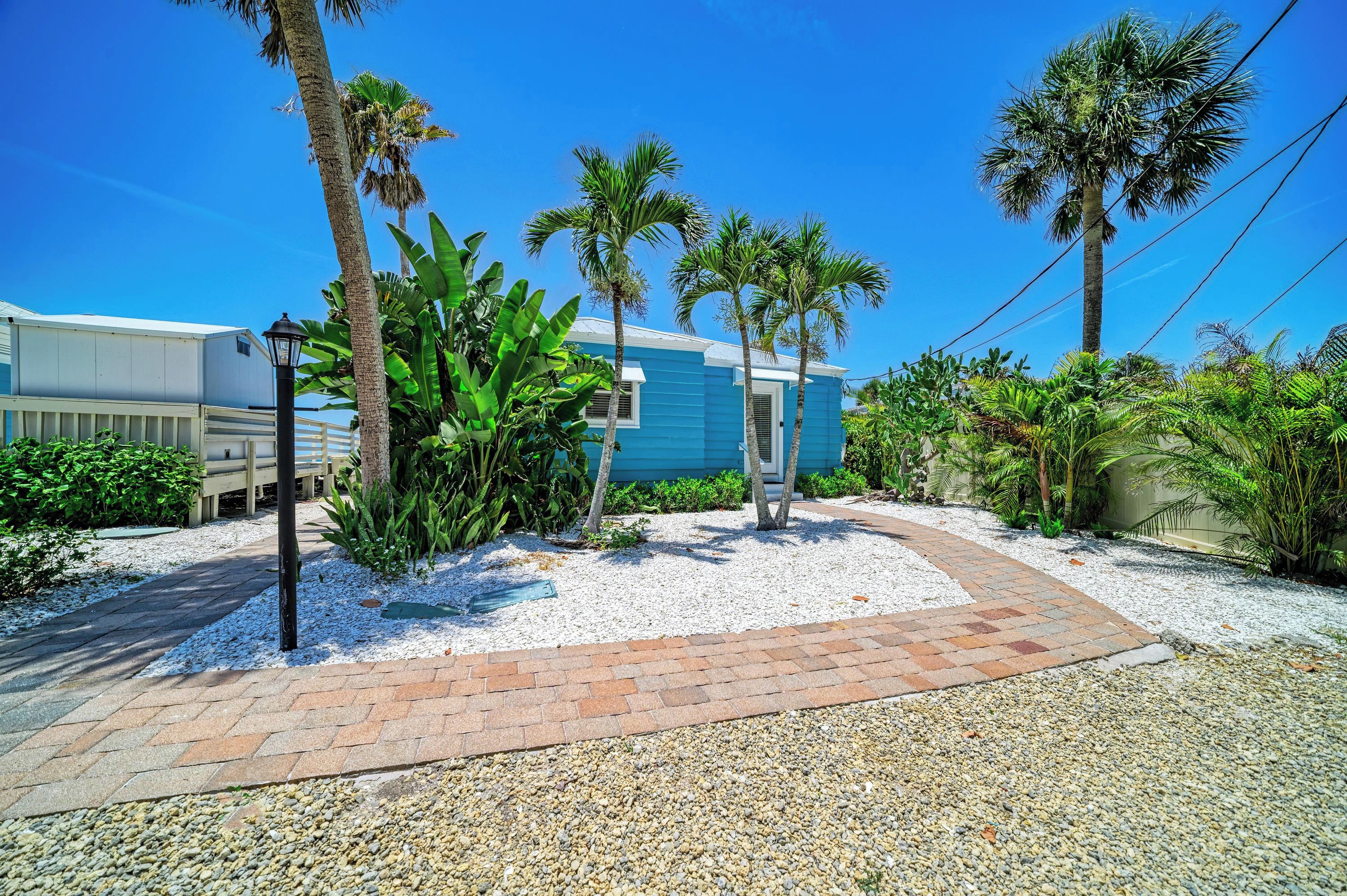 A pathway leading to a building with a blue exterior, surrounded by palm trees and various plants.