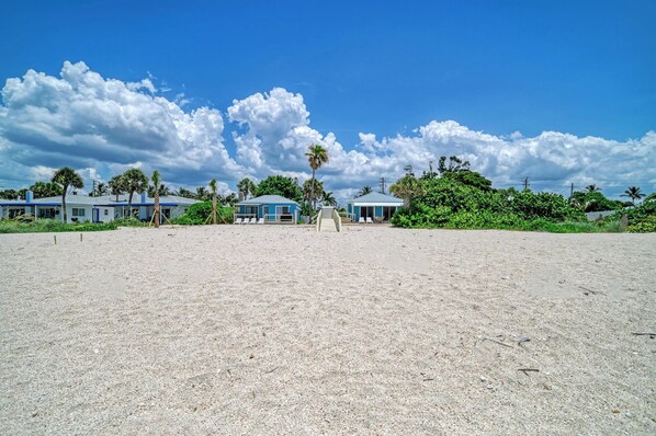 A beachfront property with multiple buildings, a sandy beach, and palm trees.