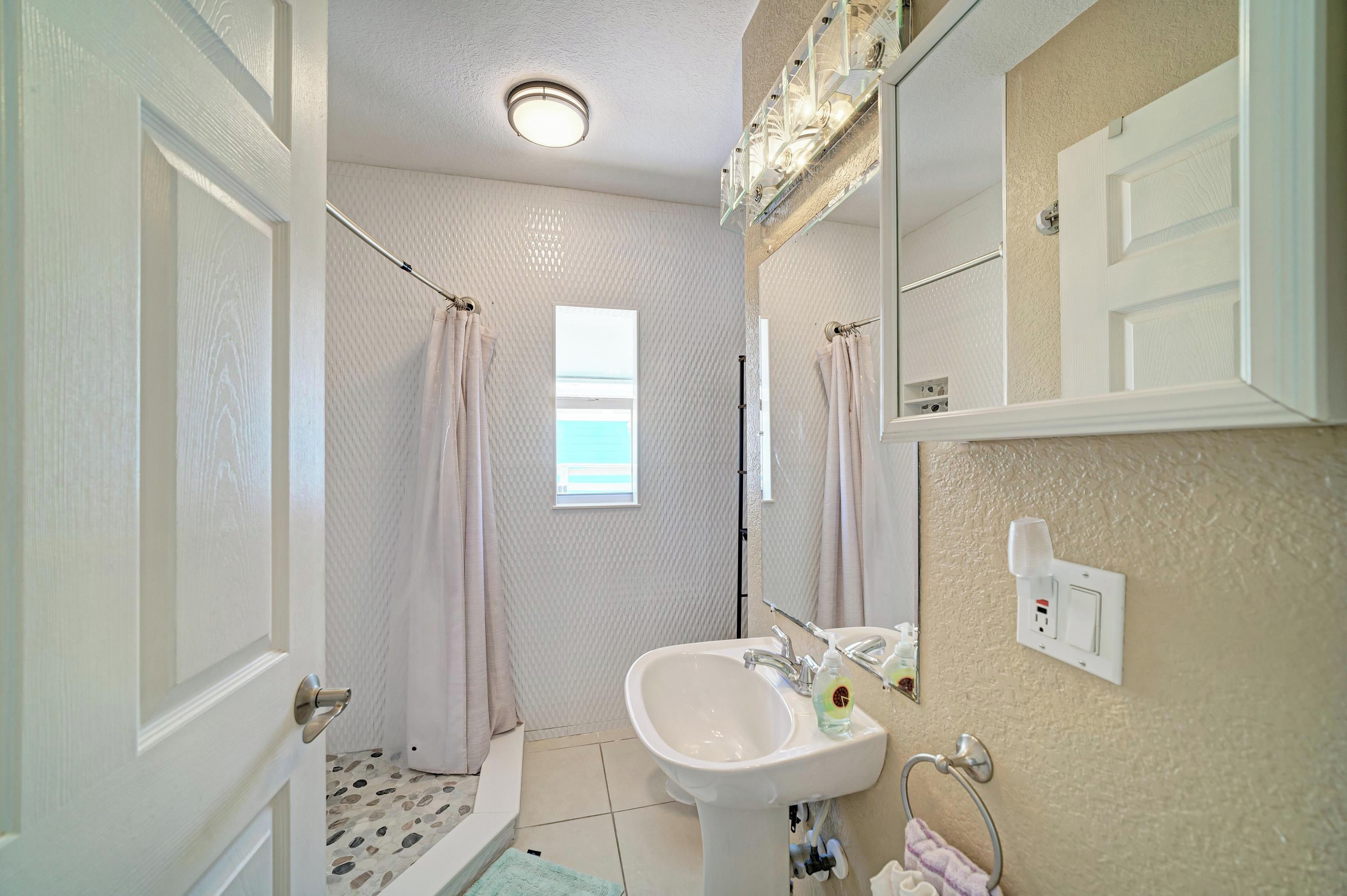 Une salle de bain avec un lavabo blanc, un miroir, un rideau de douche et une fenêtre.