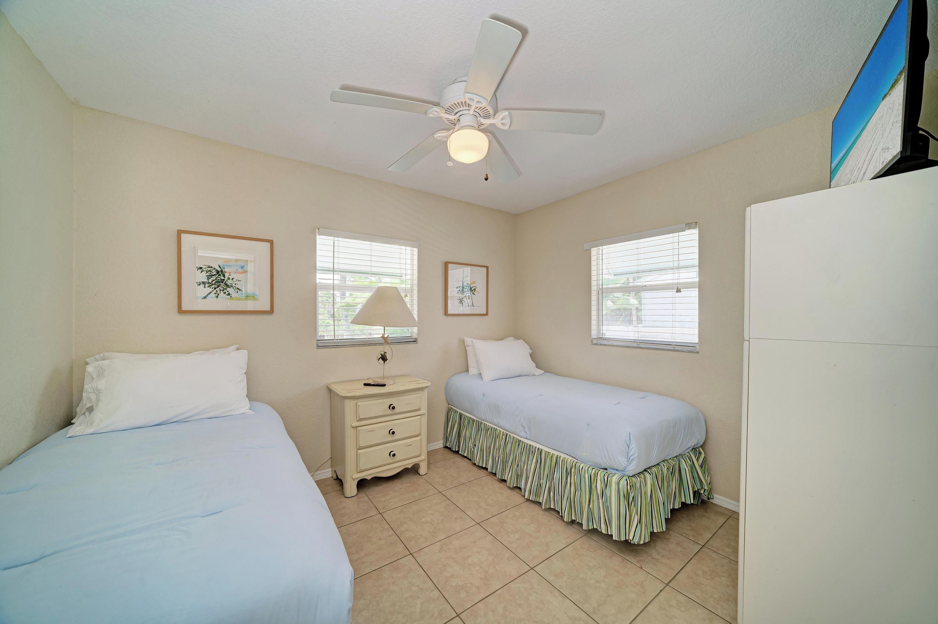 A bedroom with two beds, a ceiling fan, and a window with blinds.