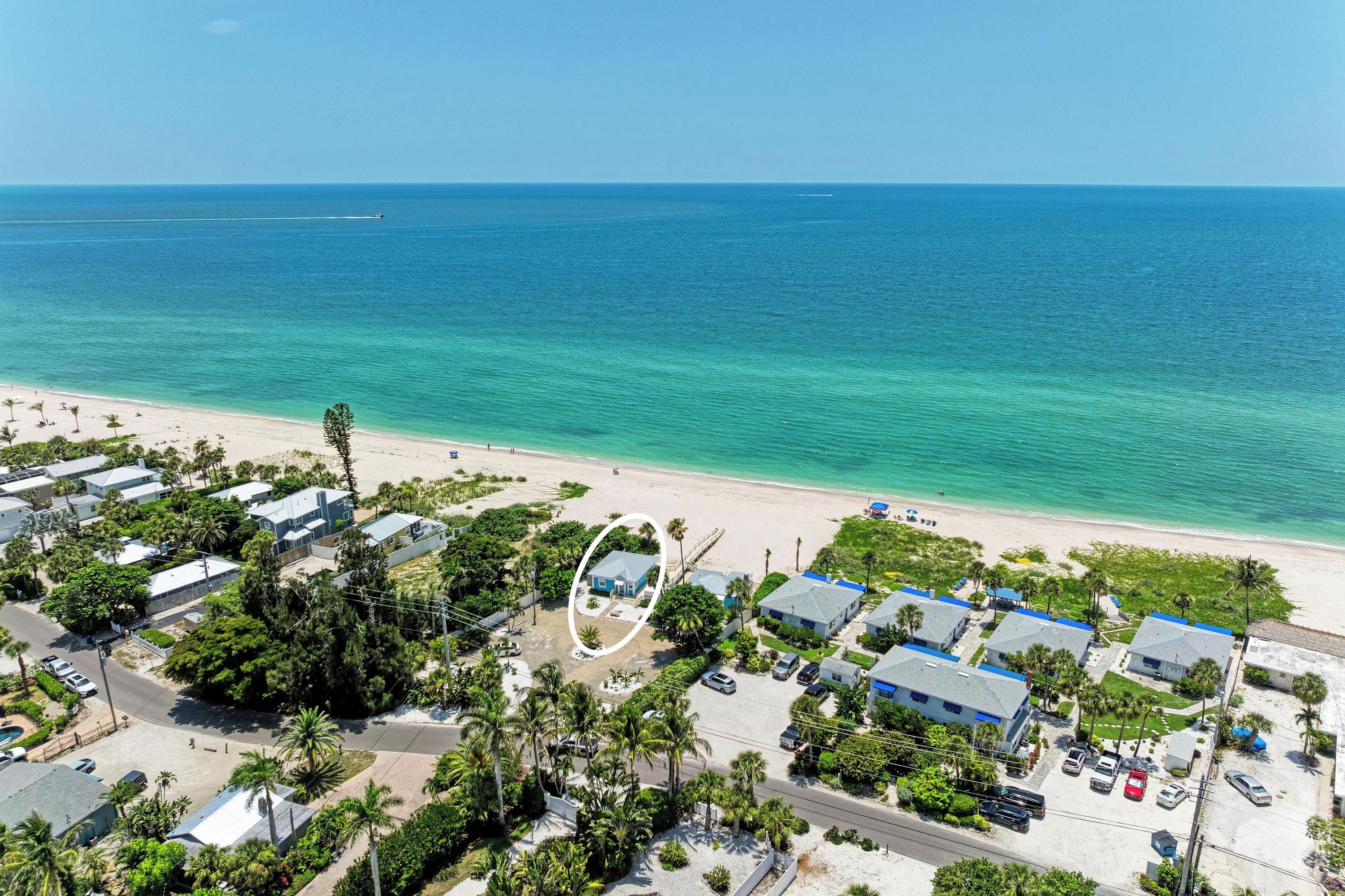 A coastal area with beach houses, clear blue sea, and a road leading to the beach.
