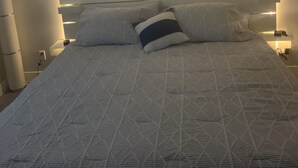 Una cama bien hecha con una colcha estampada, una obra de arte de una flor en la pared y lámparas de noche.