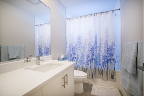A modern bathroom with a white sink, a toilet, and a shower curtain with a floral pattern. - Stay at our comfy corner! (Surrey)