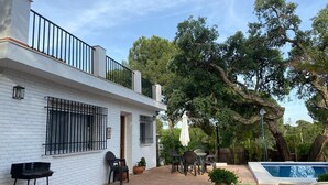 Une maison moderne avec une façade blanche, un balcon doté de rampes noires, un patio aménagé avec du mobilier d’extérieur et une piscine.