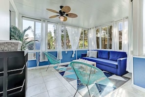A sunlit room with a blue sofa, a ceiling fan, and a large window.