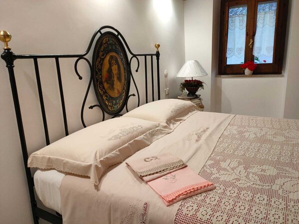 A neatly made bed with a decorative headboard, a bedside lamp, and a window with curtains. - HOLIDAY HOME Mìrame 2min. from the historic center, renovated romantic and elegant (Ovindoli)