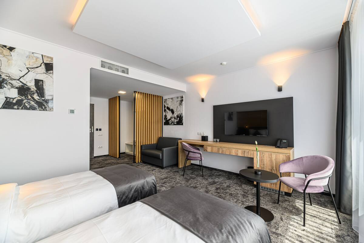A modern hotel room with two beds, a desk, a chair, and a TV.