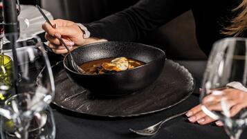 Una persona cenando en una mesa con un tazón de sopa, una copa de vino y un tenedor.