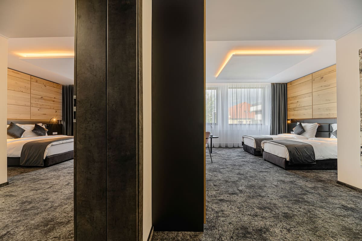 A modern hotel room with two beds, a large dark pillar, and a view of the city through large windows.