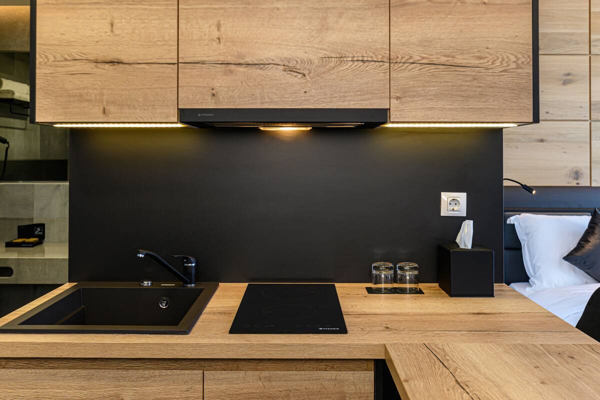 A modern kitchen with wooden cabinets, a black countertop, a sink, and a built-in induction cooktop.