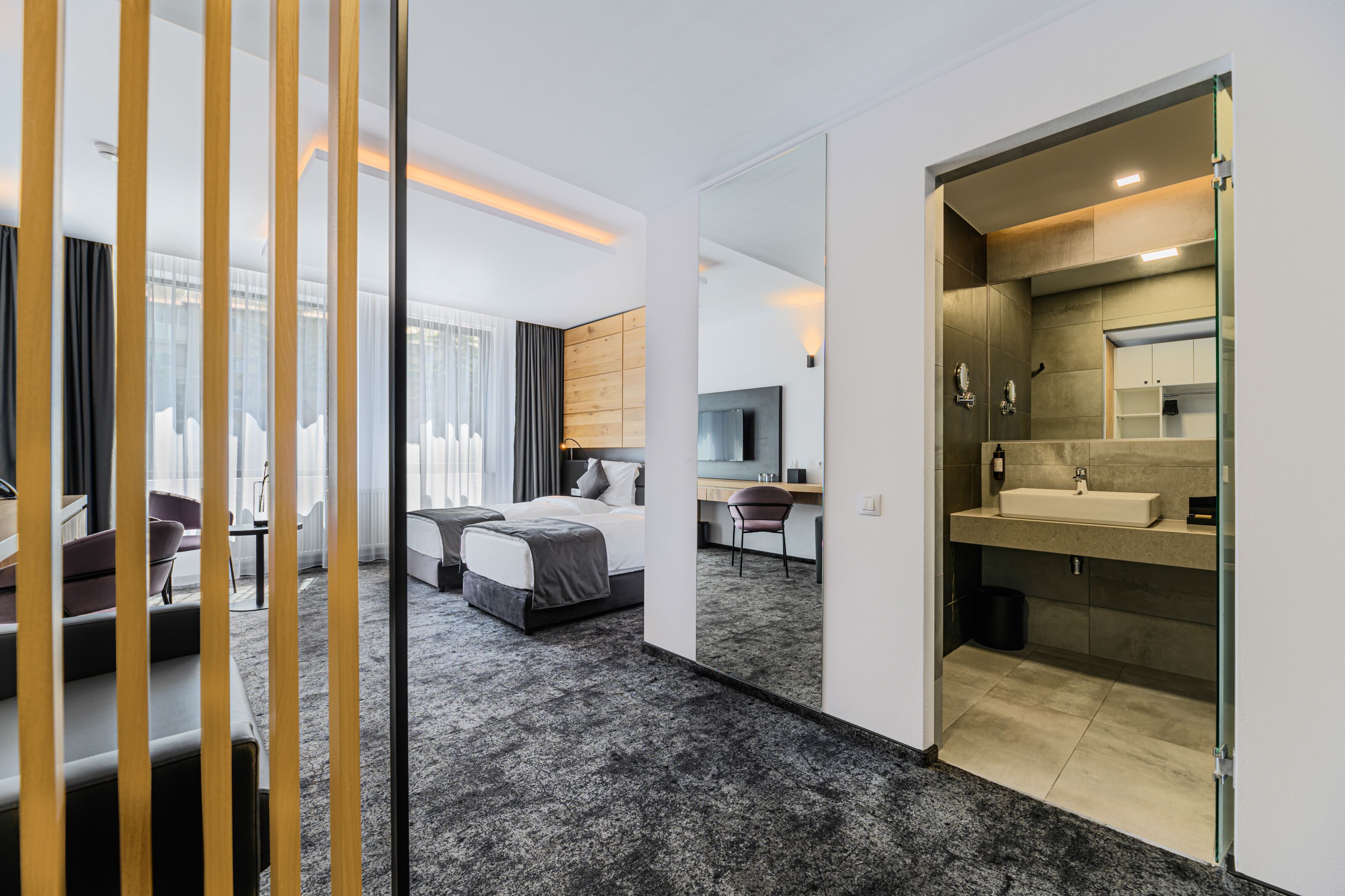 Una habitación de hotel moderna con una cama grande, un escritorio y un baño con un espejo grande y lavamanos.