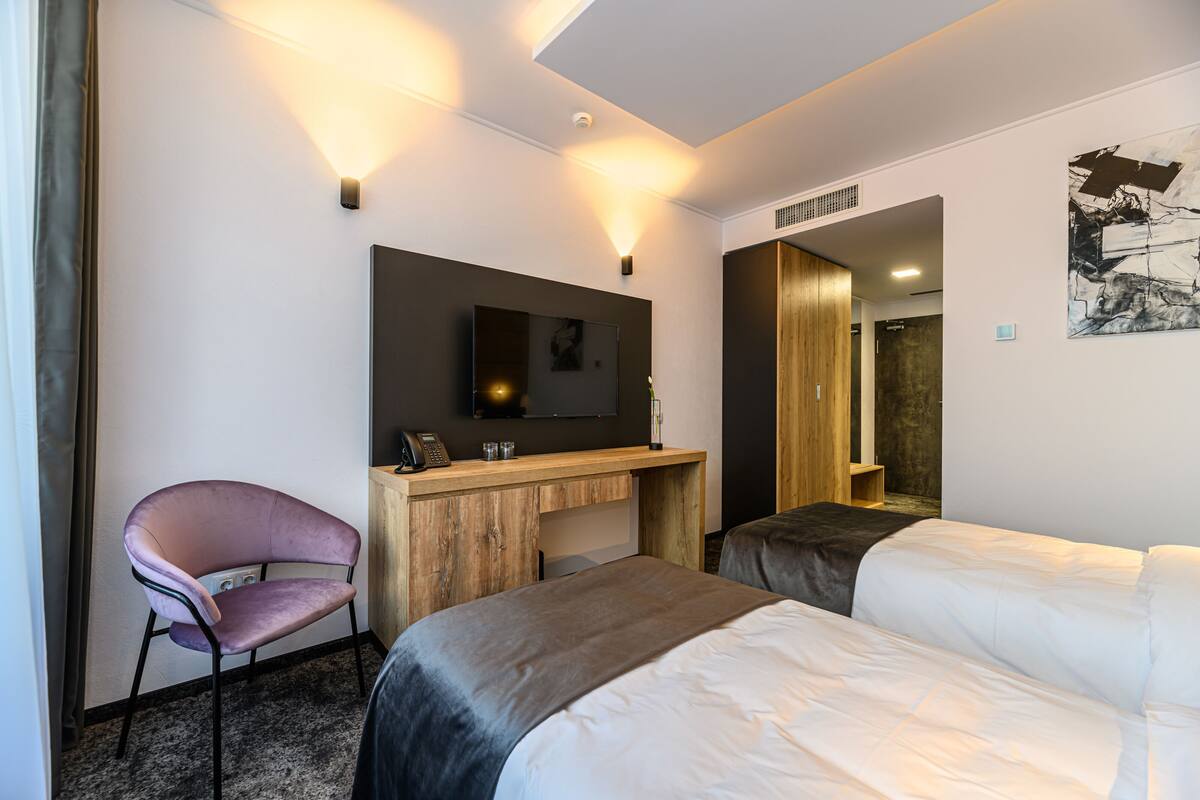 A hotel room with two beds, a desk with a flat-screen TV, a chair, and a wall-mounted artwork.