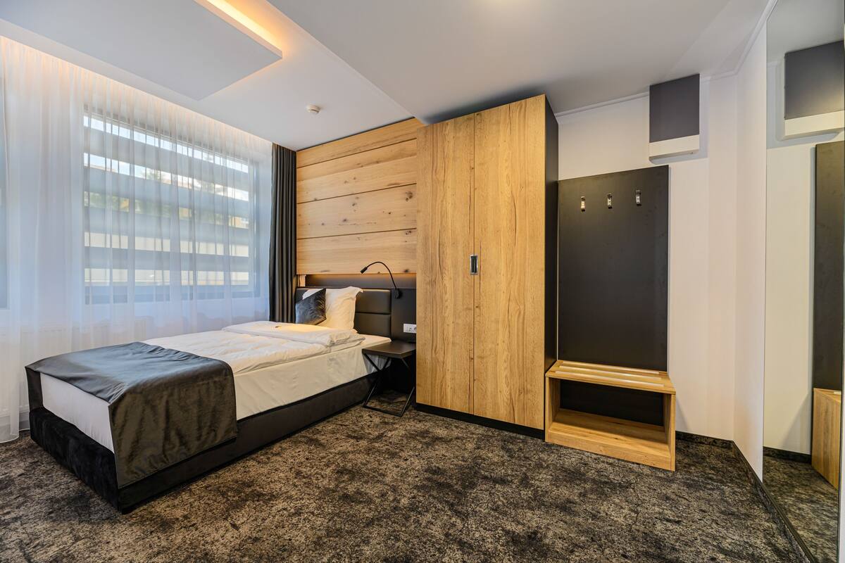 A modern bedroom with a bed, a wooden wardrobe, a bench, and a walk-in closet.