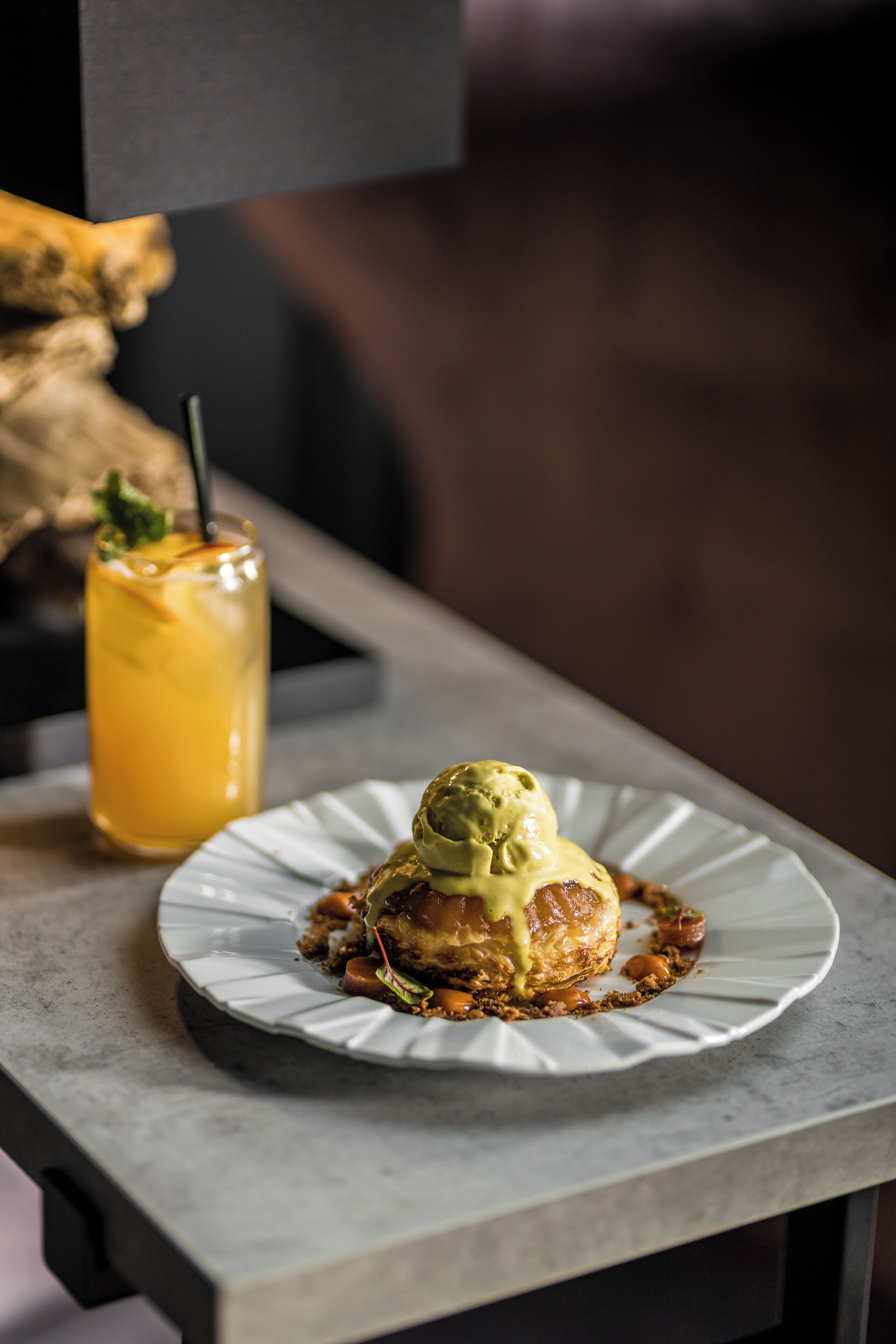 A dessert plate with a scoop of ice cream on a cookie base, accompanied by a glass of iced tea with a straw.