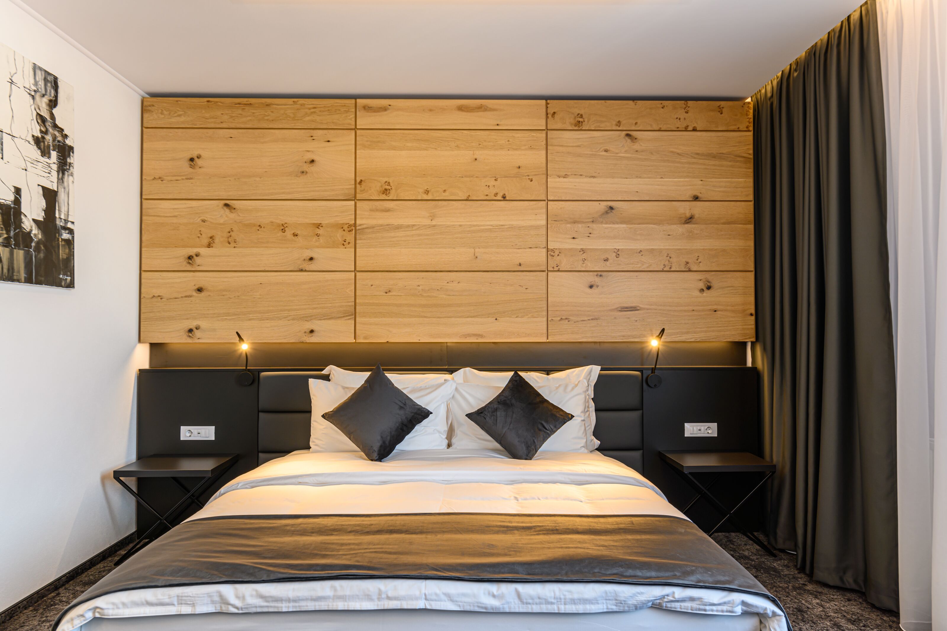 Un dormitorio moderno con cabecera de madera, una cama grande con ropa de cama blanca y negra, dos mesitas de noche y una mesita auxiliar.