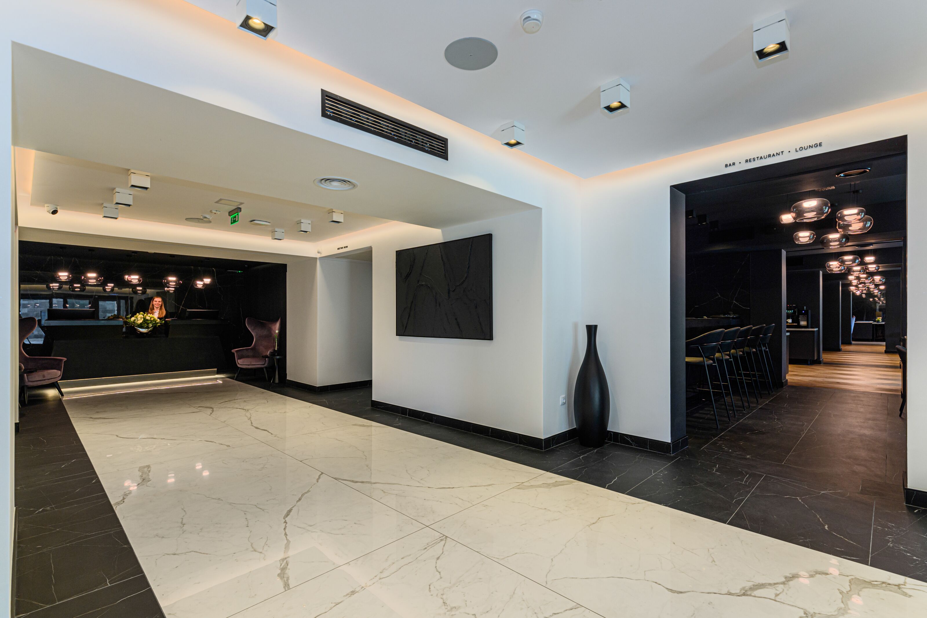 A modern hotel lobby with a marble floor, a reception desk, and a bar/lounge area.