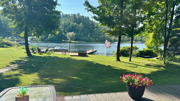 A deck with a view of a lake, a boat docked on the water, and an American flag. - Tranquil waterfront cottage in Central Lake (Central Lake)