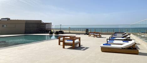 A rooftop pool area with lounge chairs and a view of the ocean.