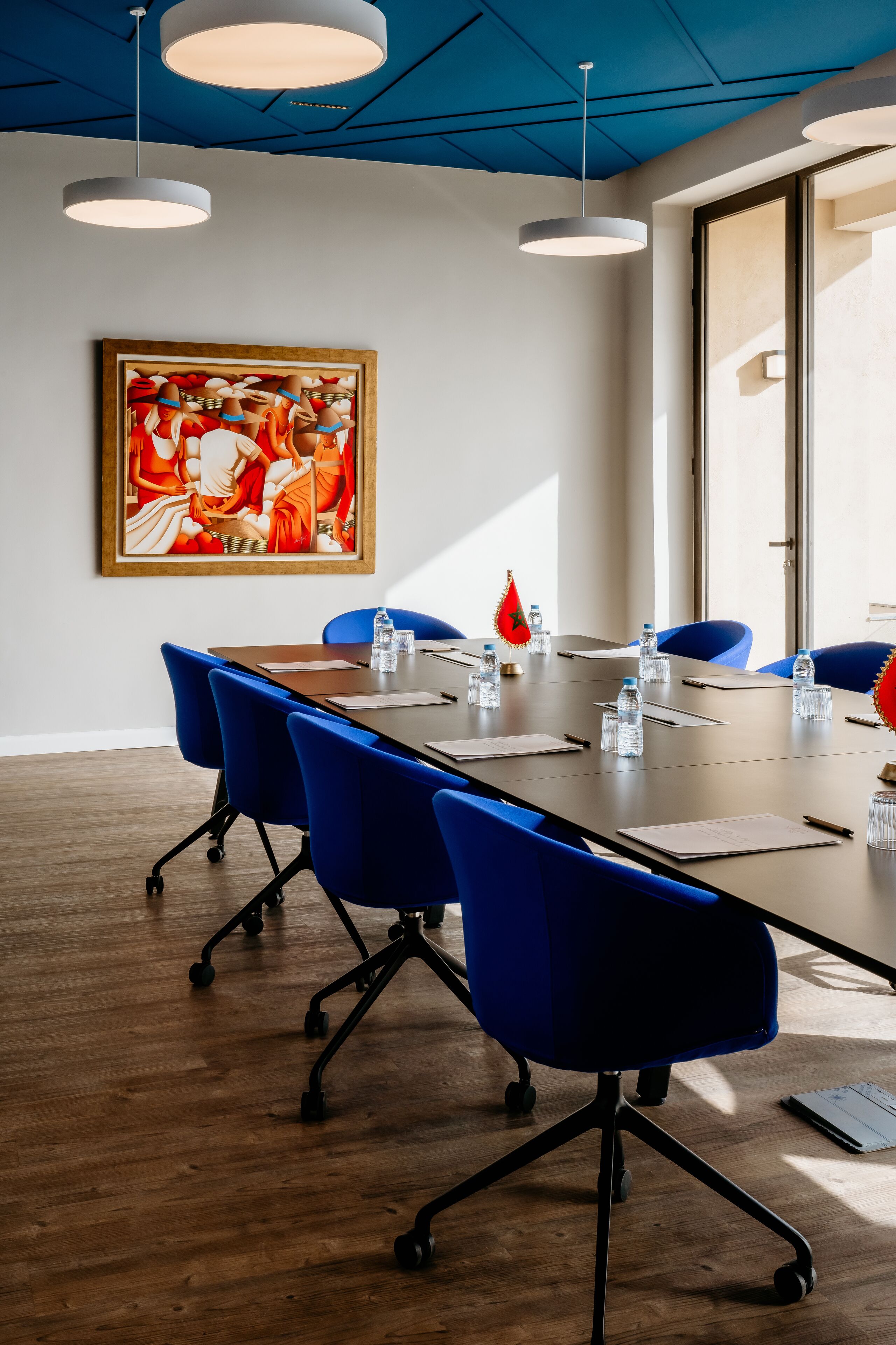 Une salle de conférence avec une longue table, des chaises bleues et un tableau accroché au mur.