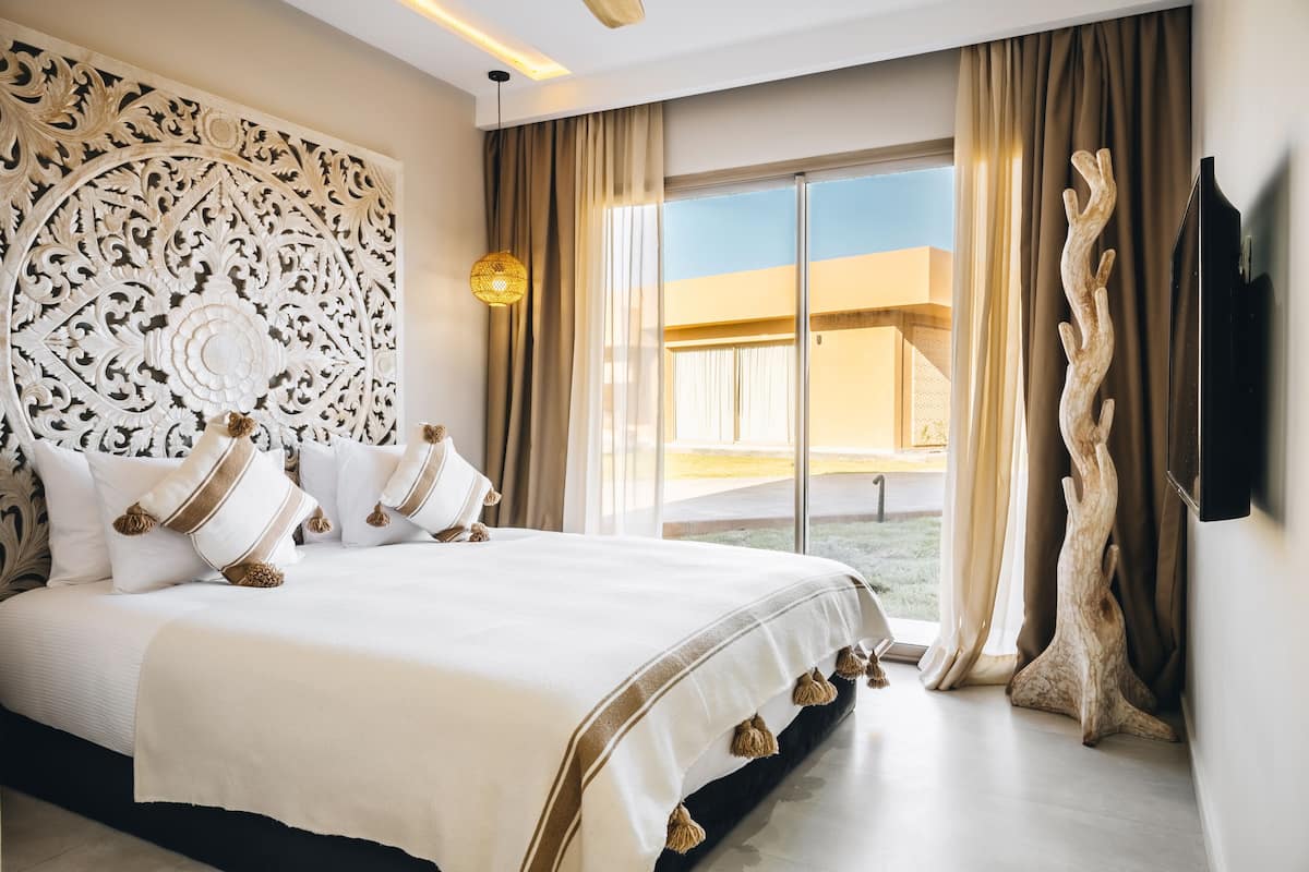 A spacious bedroom with a large bed, a decorative wall panel, a view of the outdoors, and a television on the wall.