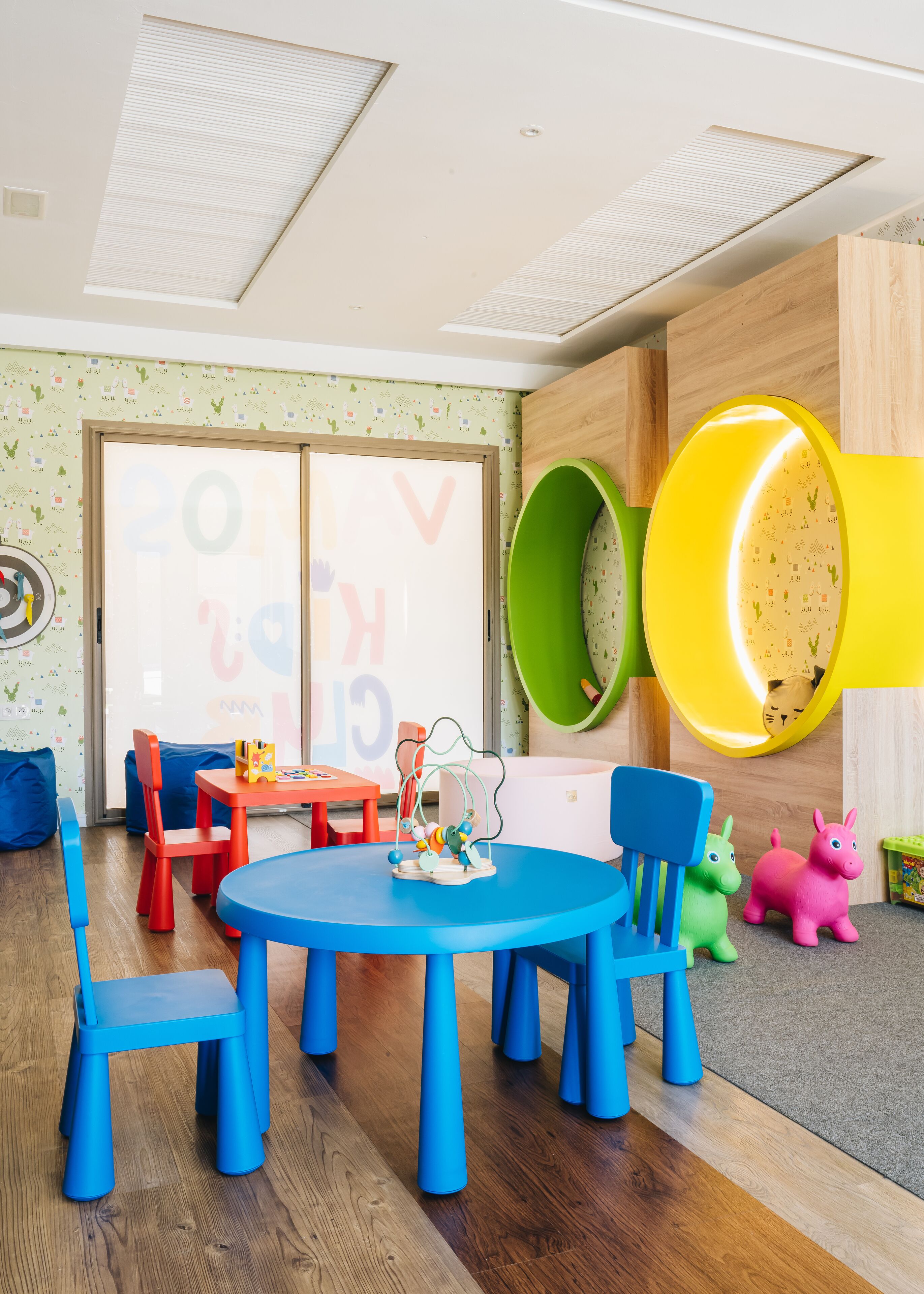 Ein Kinderzimmer mit einem runden Tisch, blauen Stühlen und bunten Spielsachen.