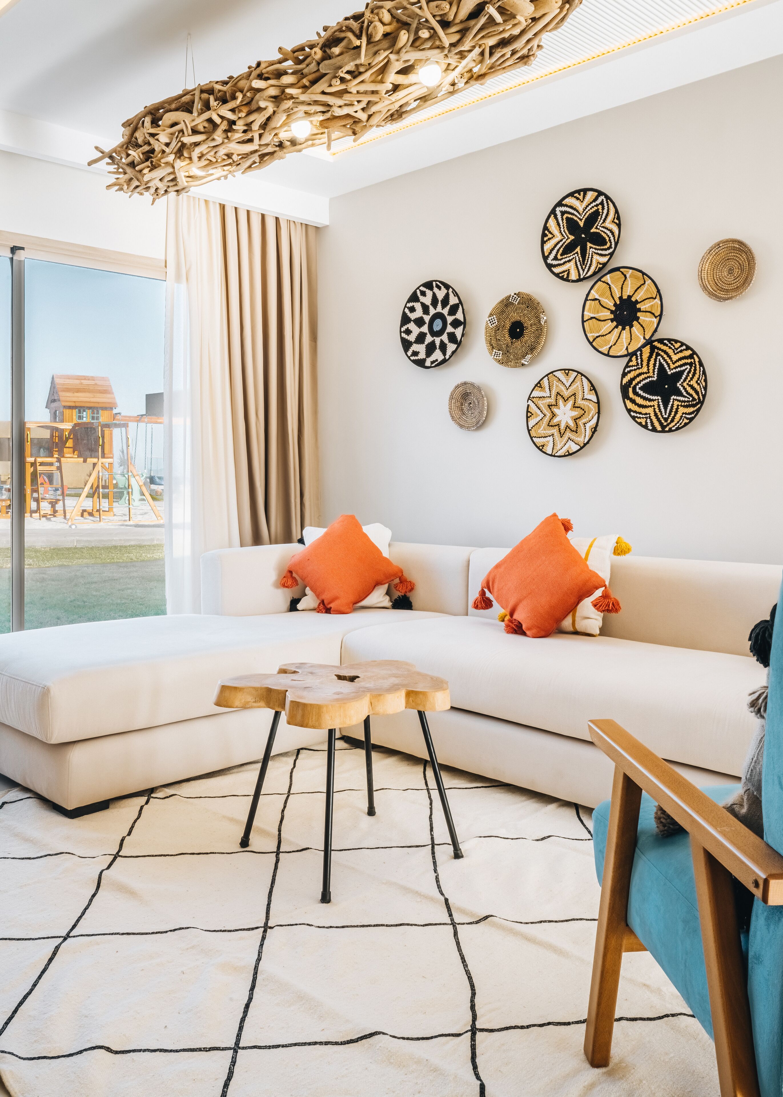 A modern living room with a white sofa, orange cushions, a wooden coffee table, and a unique ceiling light fixture.