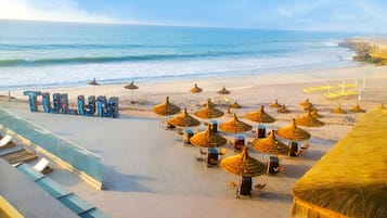 Relax by the ocean with a clear view, shaded by thatched umbrellas and surrounded by lounge chairs.