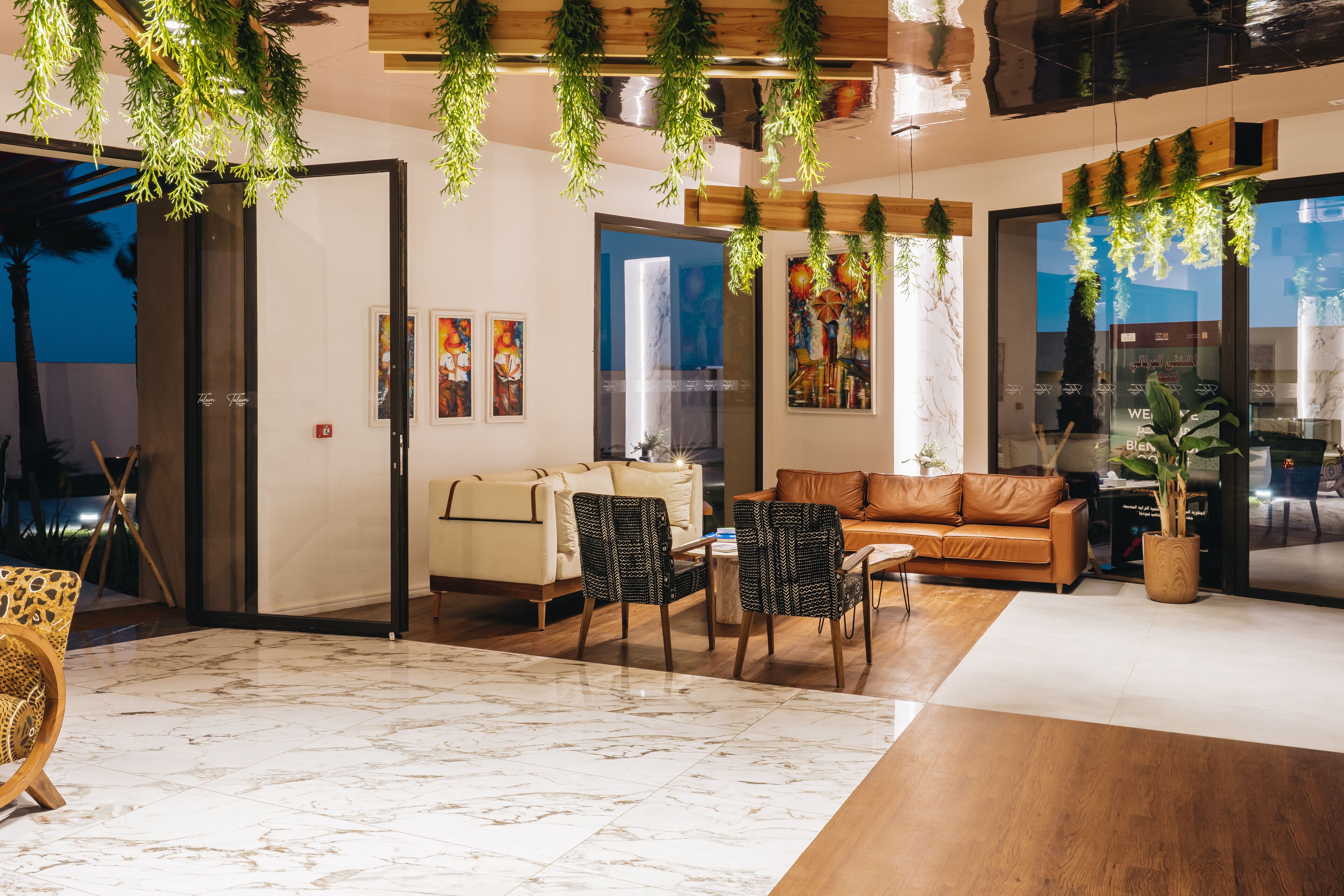 A modern living room with a sofa, chairs, a dining table, and hanging plants.