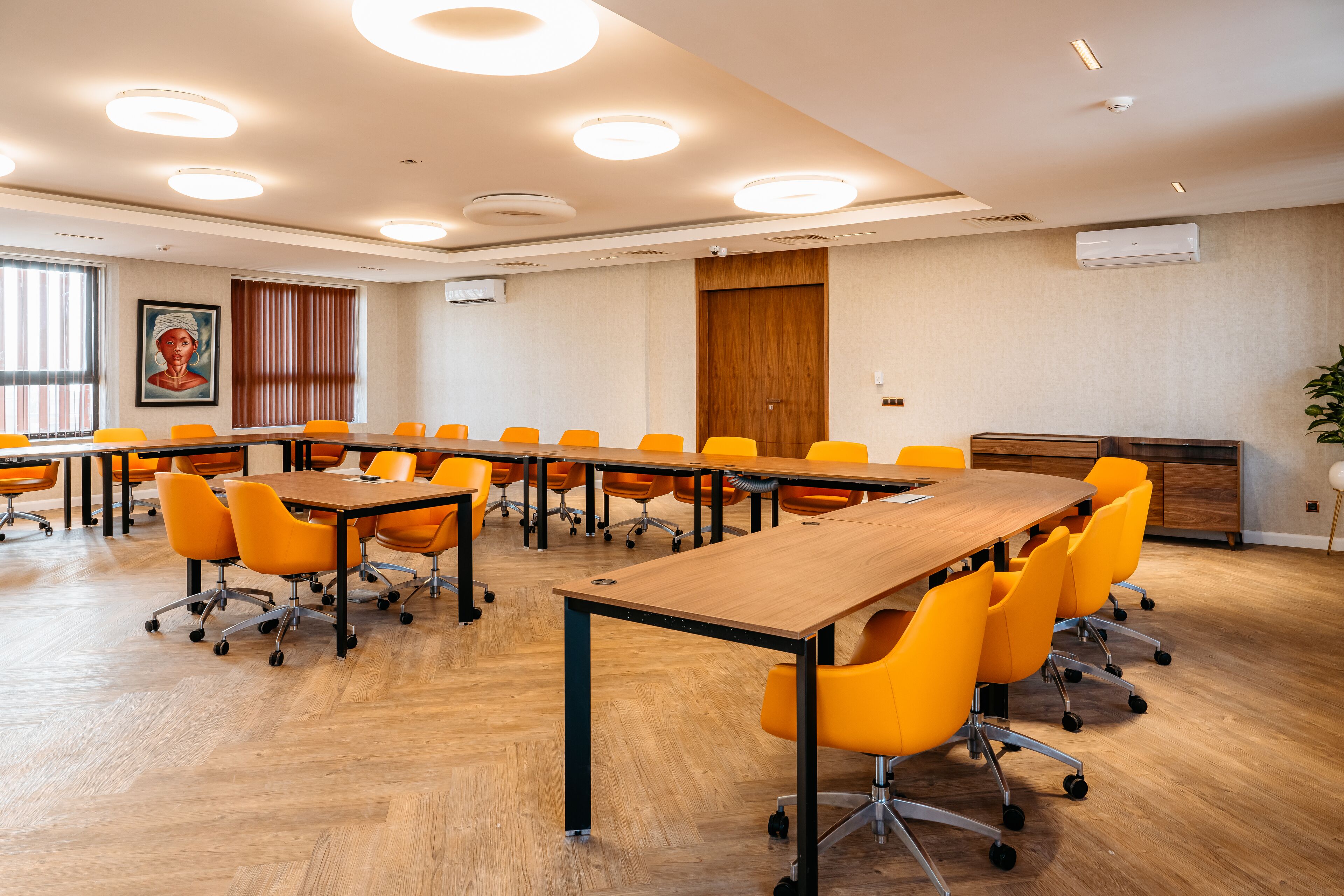 Uma sala de conferências com uma mesa comprida, cadeiras laranja e piso de madeira.