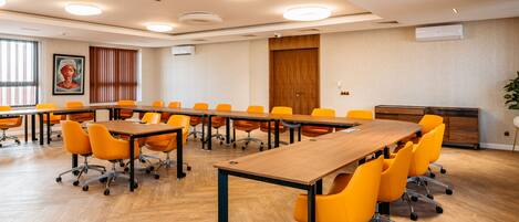 Uma sala de conferências com uma mesa comprida, cadeiras laranja e piso de madeira.