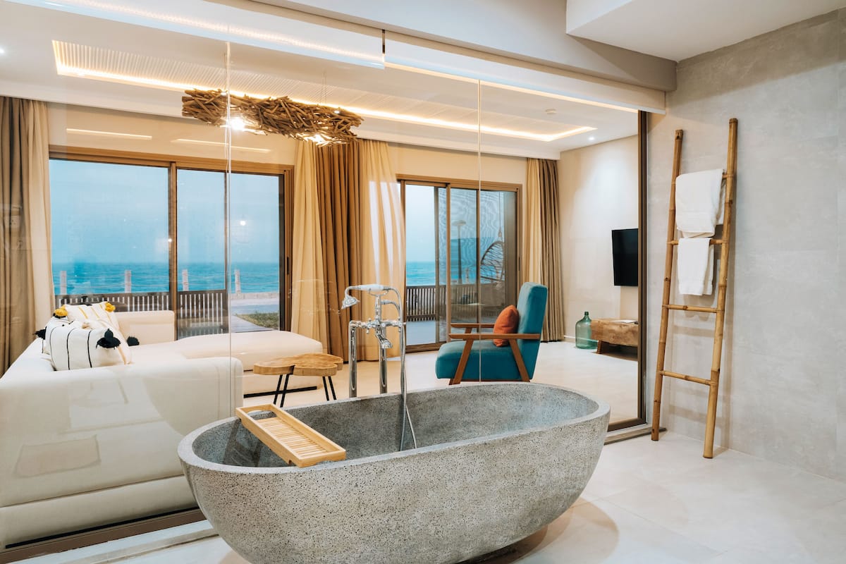 A modern bathroom with a freestanding bathtub, a sofa, and a view of the sea.